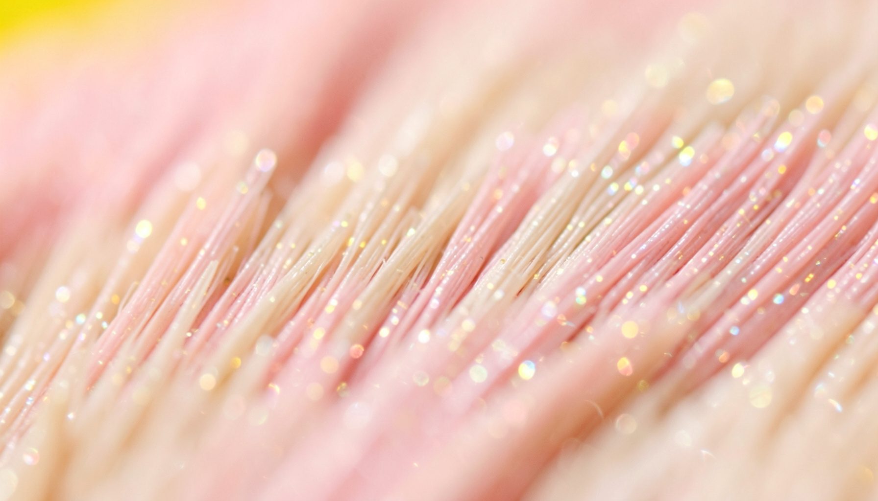 Primer plano extremo de una textura de brochas de maquillaje con cerdas sintéticas en tonos rosa pálido, beige y destellos nacarados, sobre un fondo suave y difuminado.